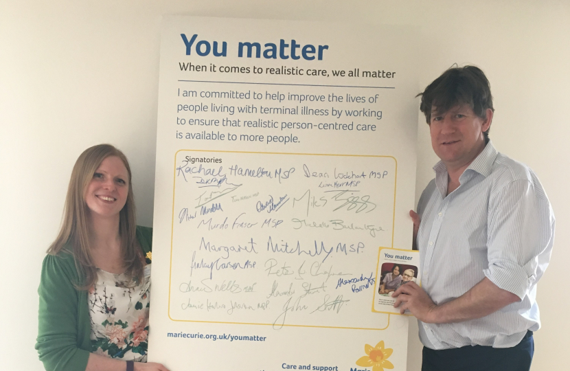 Alex and a representative from Marie Curie holding a poster between them.