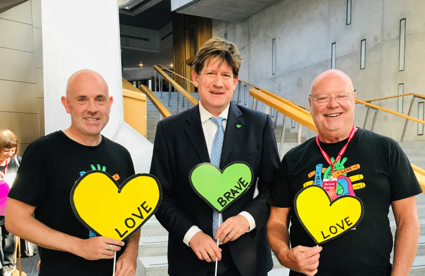 Alex is standing holding a heart shaped cut out with two representatives from Heart Research UK.