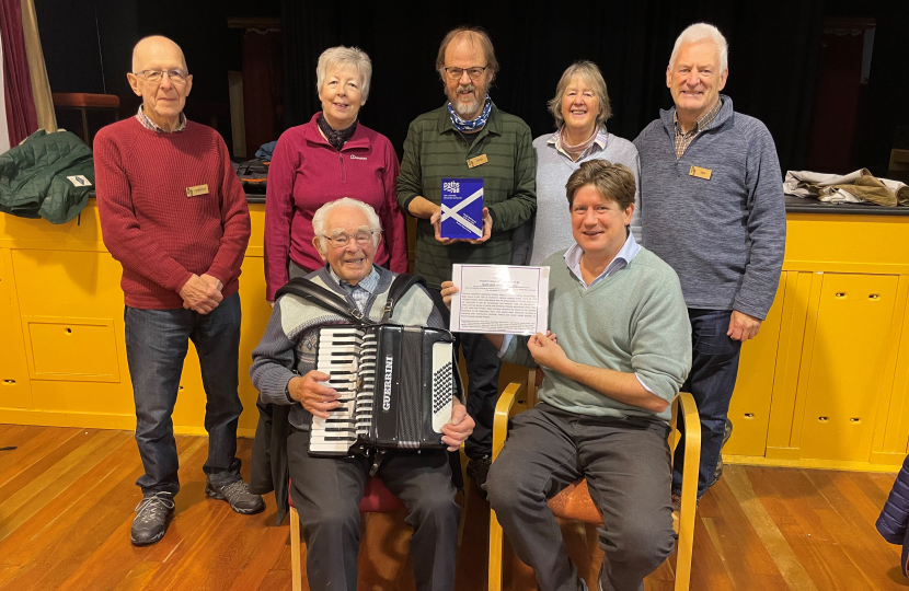 Alex, seated, holding a certificate of recognition with six members of Positive Steps Kemnay.