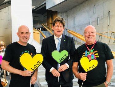 Alex is standing holding a heart shaped cut out with two representatives from Heart Research UK.