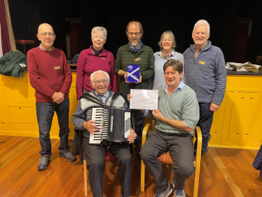 Alex, seated, holding a certificate of recognition with six members of Positive Steps Kemnay.